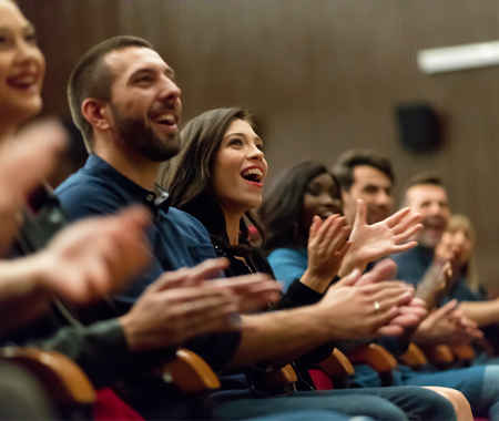 A crowd laughs and claps in a theatre